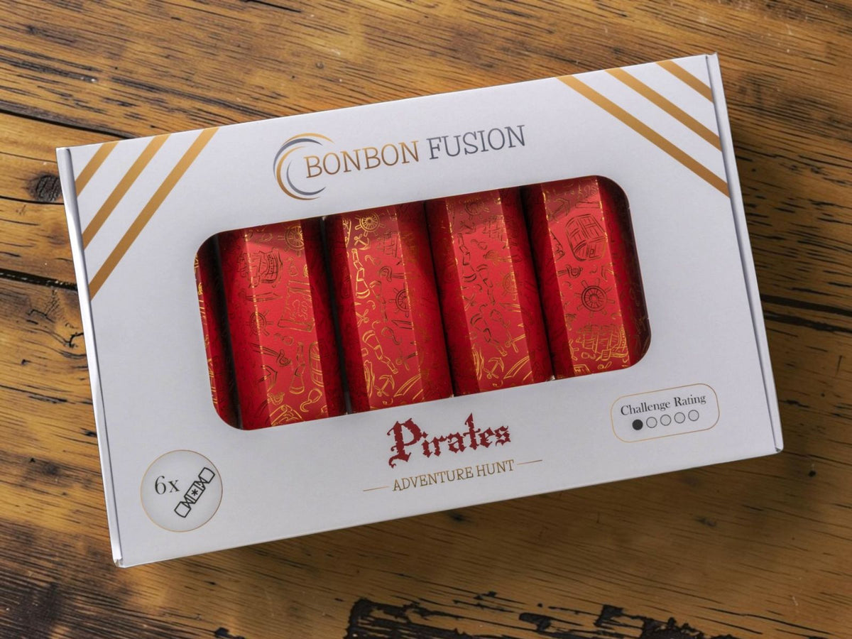 Bonbon Fusion Adventure Hunt Pirates pack with six red and gold illustrated Christmas bonbons, displayed in a white presentation box on a rustic wooden table.