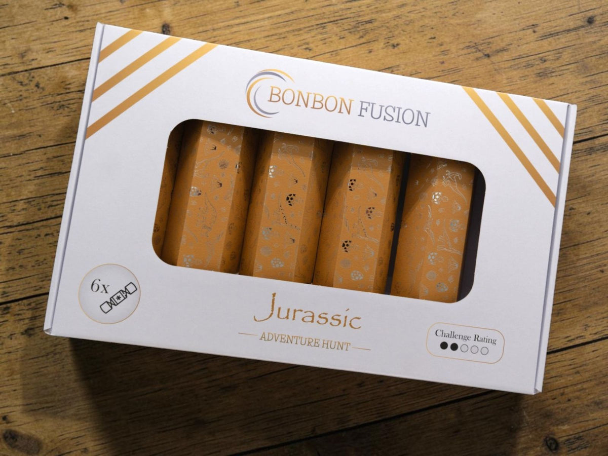 Bonbon Fusion Adventure Hunt Jurassic pack featuring six orange bonbons with dinosaur tracks and fossil-inspired illustrations, displayed in a white presentation box on a rustic wooden table.