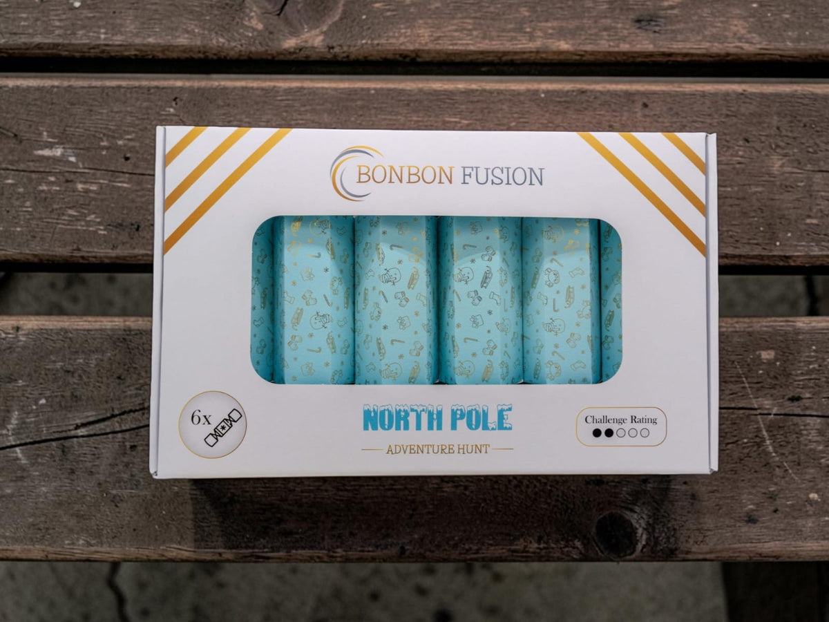 Bonbon Fusion North Pole Adventure Hunt pack of six light blue Christmas bonbons with gold festive designs, in a white and gold box on a wooden bench