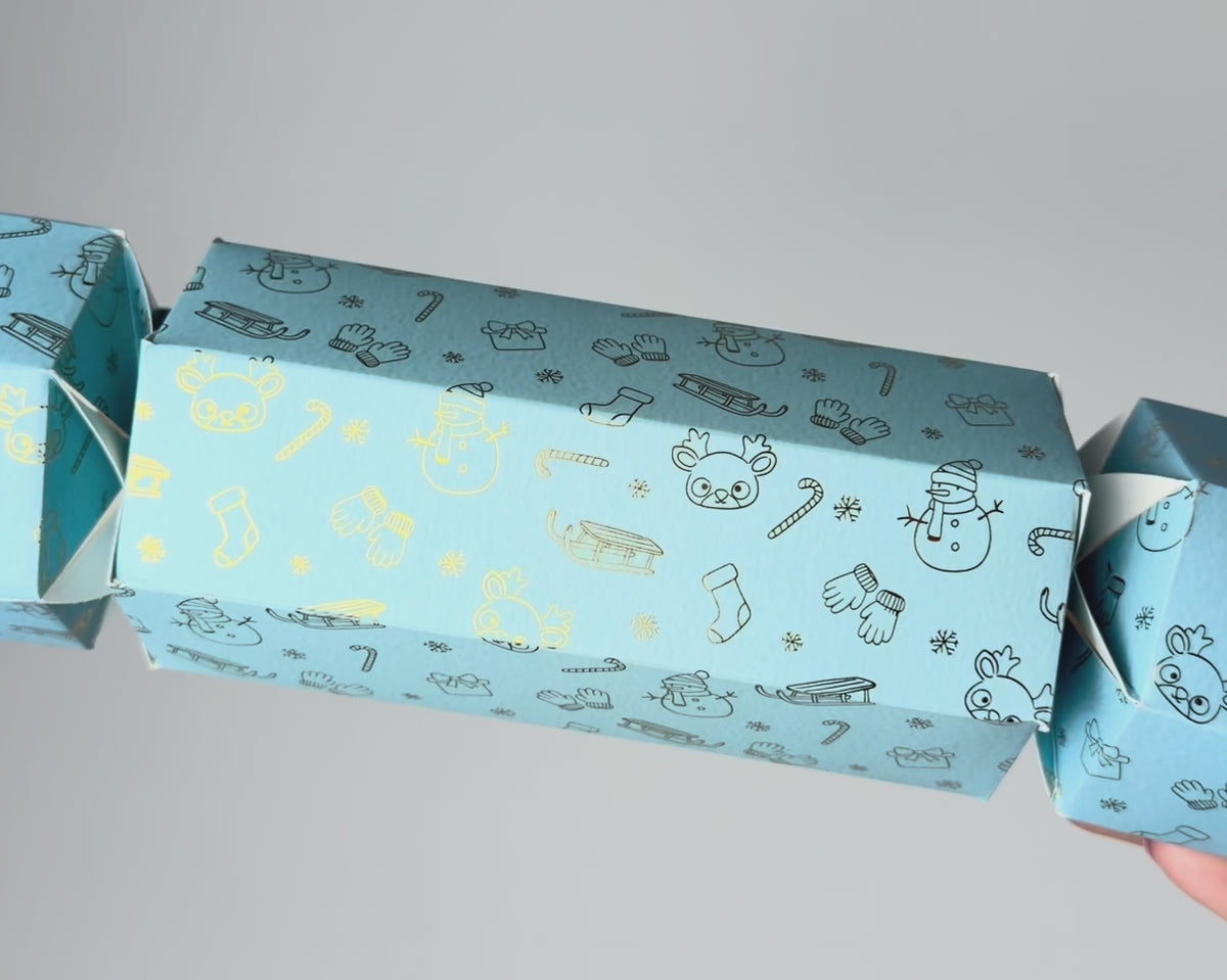 Close-up video of a light blue North Pole Christmas bonbon, showing its hexagonal shape and metallic festive designs of reindeer, snowmen, sleighs, stockings and snowflakes.