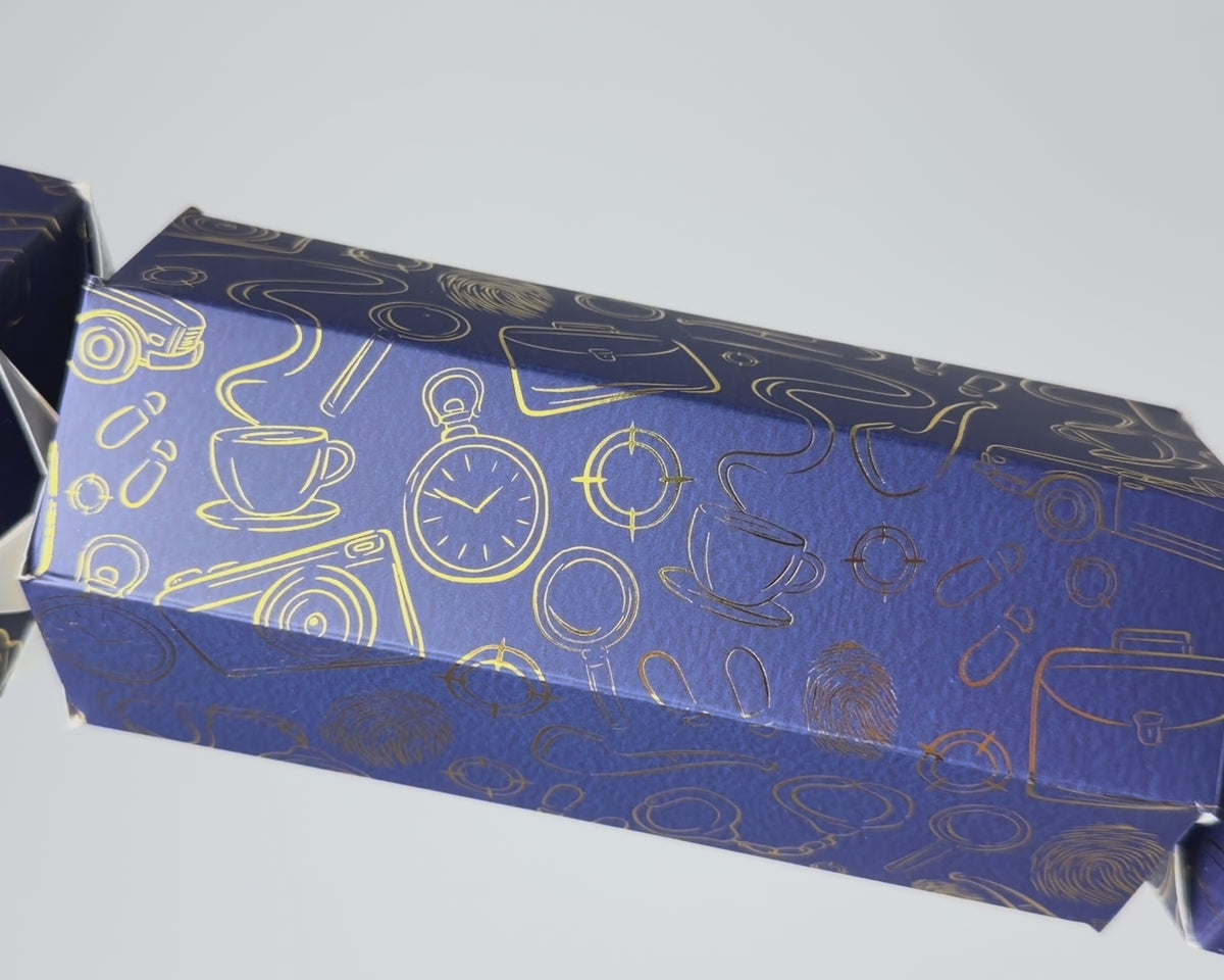 Close-up video of the Bonbon Fusion Spies Christmas bonbon showing its navy textured card and shimmering gold foil spy illustrations, including a pocket watch, teacup, camera, magnifying glass and fingerprints