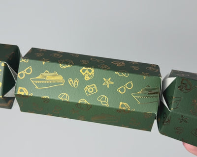Close-up video of a dark green Holiday Cruise Christmas bonbon, showing its hexagonal shape and gold foil designs of cruise ships, anchors, starfish and holiday accessories.