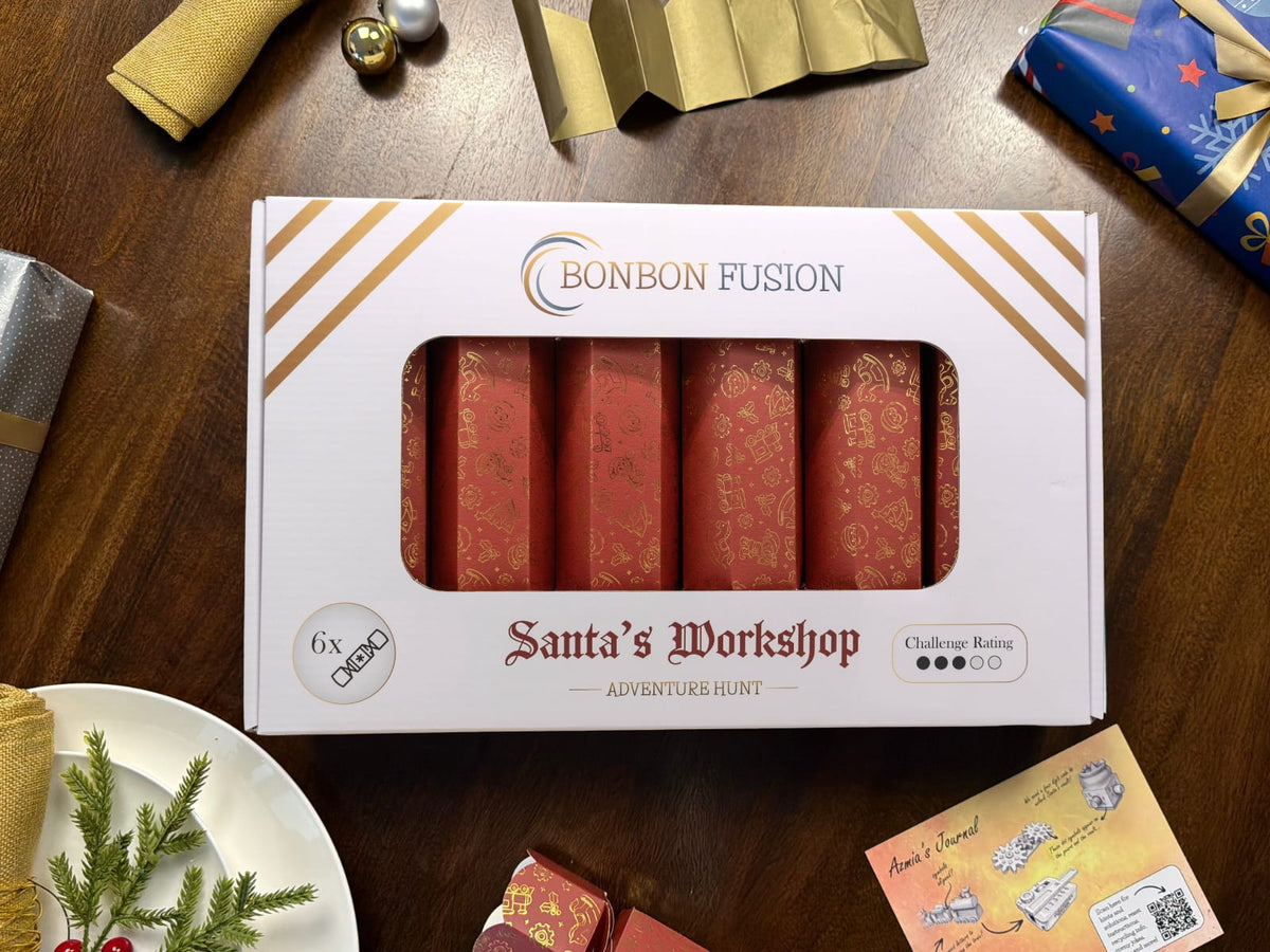 Bonbon Fusion Santa’s Workshop Adventure Hunt pack of six red and gold Christmas bonbons on a wooden table, surrounded by wrapped gifts, festive tableware, a gold paper crown and Azmia’s journal card.
